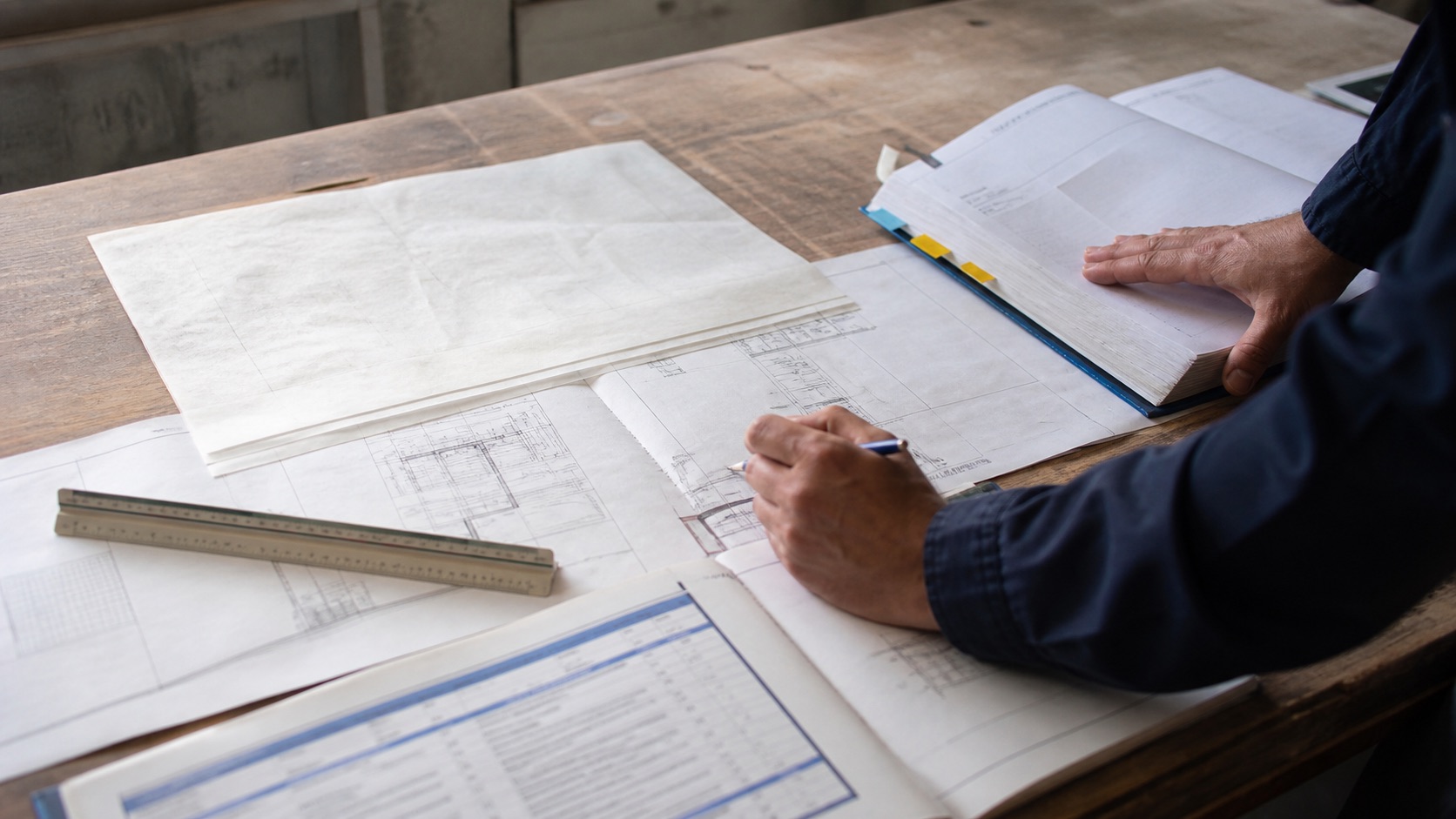 Project manager comparing drawings, specifications, and a scope worksheet during a construction package review.